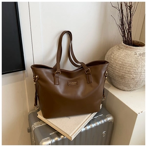 Detail view of large dark brown tote bag with leather logo patch and metal hardware
