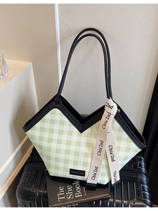 Green Vichy check tote bag with black leather straps and decorative ribbon on suitcase