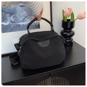 Dettaglio borsa a mano in nylon nero con targhetta logo in pelle e ampia tracolla