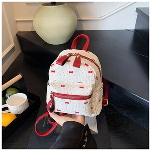 Close-up of knit mini backpack with red bow patterns and leather straps in a home setting