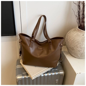Detail of a brown leather tote bag showing the gold logo and metal side buckle