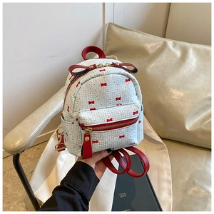 Detailed view of white mini backpack with red bow patterns and leather accents