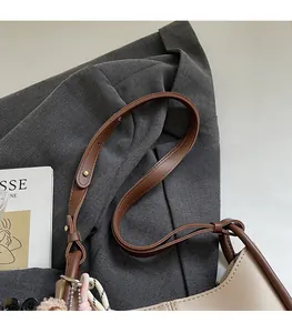 Détail du sac cabas beige avec bandoulière marron, pompon rose et pendentif tressé
