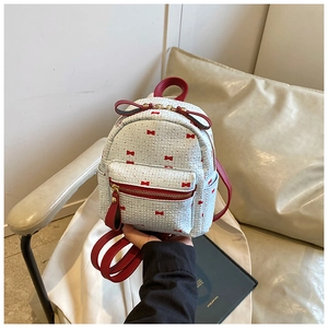 Detail of white mini backpack with honeycomb texture and red bow print highlights