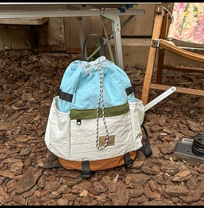 Outdoor camping scene showing a color-block drawstring backpack made of lightweight nylon