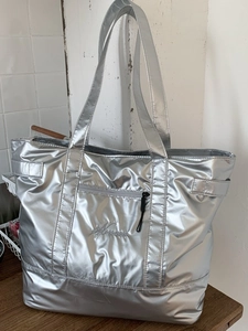 Grand sac cabas argenté métallisé avec larges anses et poche zippée sur un plateau bois