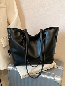 Black large capacity faux leather tote bag with gold hardware on a silver suitcase