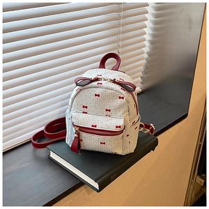 Close-up of sweet white backpack with red ribbon patterns on a stack of black books