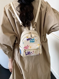 Mini sac à dos beige avec graffiti de chat et zips dorés porté sur un trench chic