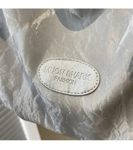 Close-up of the silver metallic fabric texture and brand logo patch on the tote bag