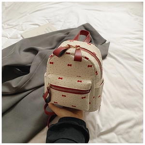 Detail of cream mini backpack with red bow pattern and textured faux leather finish