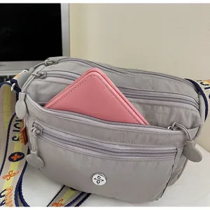 Detail view of grey nylon crossbody bag showing multiple zip layers and interior storage