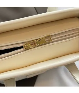 Close-up of polished gold-tone zipper puller on a cream-colored leather tote bag detail