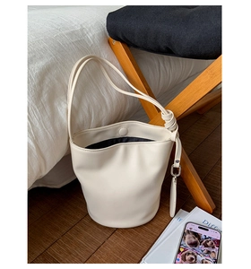 Detail der weißen Beuteltasche mit Knotendekor und Doppelgurt vor schlichtem Wohnzimmer
