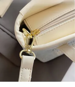 Detail of cream white bucket bag featuring a gold metal hook and zipper closure
