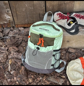 Close-up of green hiking backpack with mesh pocket and orange zippers on wood background
