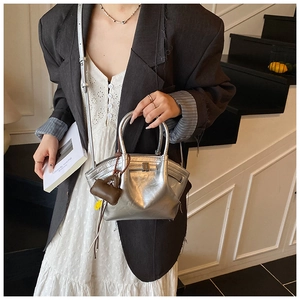 Chic silver metallic dumpling bag with buckle detail held by a model in a black suit