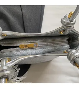 Gros plan du sac seau en cuir argenté avec fermeture éclair dorée et sangle à motif noué
