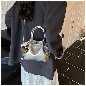 Detailed view of metallic silver dumpling bag with gathered folds and dark brown charm