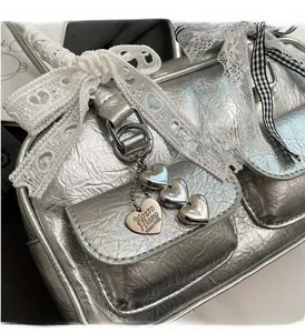 Detail of silver metallic handbag featuring lace bows and engraved heart pendant