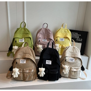 Close-up of canvas backpacks in six colors with teddy bear charms and logo patches