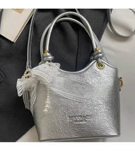 Détail du sac argenté texture craquelée avec nœud en dentelle et pendentif en perle