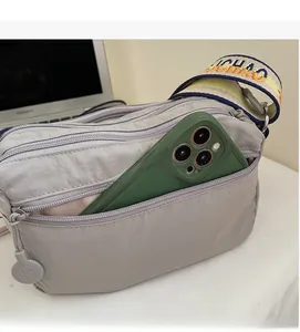 Detail view of grey nylon crossbody bag with multi-zip pockets and wide woven strap