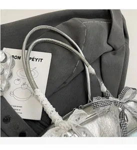 Detail of silver pleated handbag with white lace handle and black gingham bow charm