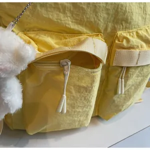 Detail of yellow nylon backpack featuring smooth white zippers and a cute plush bear charm