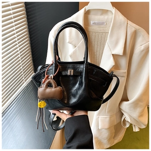 Detail of black matte leather handbag with metal buckle and decorative bag charm