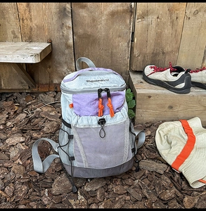 Detail of outdoor backpack featuring purple pocket, orange zipper pull, and grey nylon texture