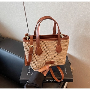 Detailed view of woven straw bag texture with brown leather straps and gold metal hardware