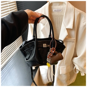 Detail of black leather dumpling bag with metal buckle and vibrant decorative pendants