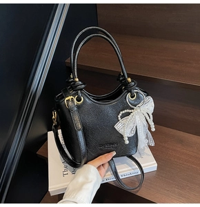Détail du sac seau noir texturé avec nœud en dentelle blanche et breloque en perles