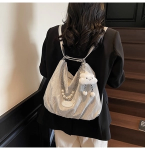 Détail d'un sac à dos plissé argenté avec chaîne de perles et breloque nuage sur blazer