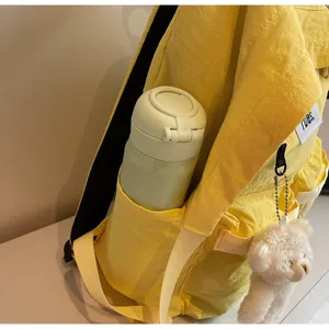 Detail view of yellow nylon backpack side pocket holding a bottle with a bear charm