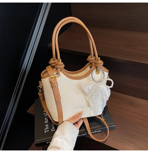 Détail du sac seau crème avec bordure marron et breloque nœud en dentelle et perles