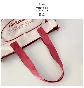 Close-up of canvas tote bag showing wide red woven handles and front zipper pocket detail