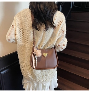Sac Hobo en cuir marron avec pendentif ours et logo doré porté sur un pull beige