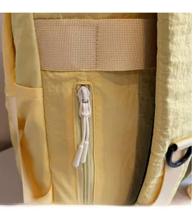 Close-up of yellow canvas backpack showing smooth zipper with white decorative cords