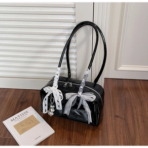 Detail of black patent leather shoulder bag with lace bow and silver heart pendant