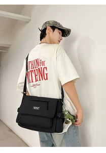 Detail view of black nylon messenger bag with green dinosaur charm and logo patch