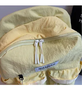 Detail of yellow nylon backpack featuring dual white zippers and woven brand label