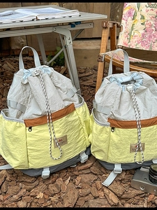 Outdoor camping scene showing large drawstring nylon backpacks in yellow and beige