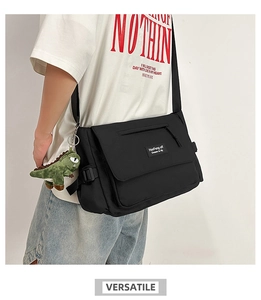 Close-up of black nylon messenger bag featuring a green dinosaur plush charm on the strap