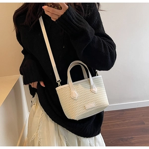 Detail of cream knit bucket bag with leather handle and brand tag on a stylish model
