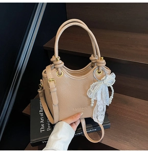 Détail du sac seau beige avec texture litchi, breloque perle et nœud en dentelle