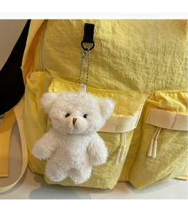 Close-up of white plush bear keychain accessory on a yellow multi-pocket backpack