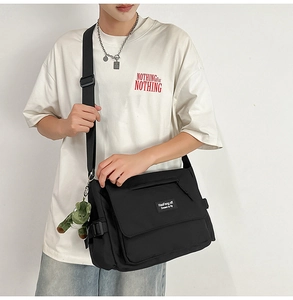 Close-up of black nylon messenger bag featuring a green crocodile plush charm and logo label