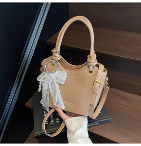 Détail du sac à main plissé beige avec anses nouées et breloque perle en dentelle